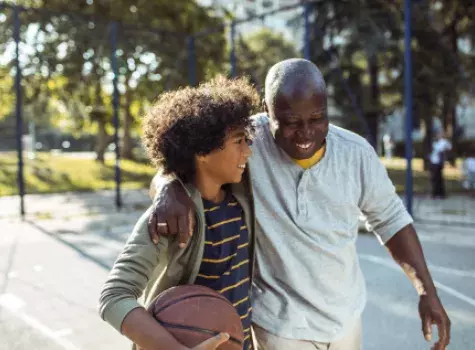 Smiling Grandfather Hugging Grandson on Outdoor Basketball Court