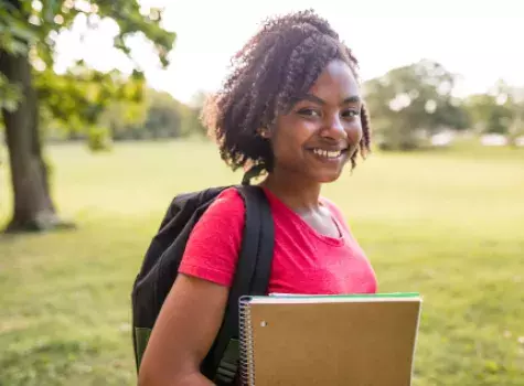 Smiling Young Black Female Student Wearing Backpack and Holding Books - Outdoors