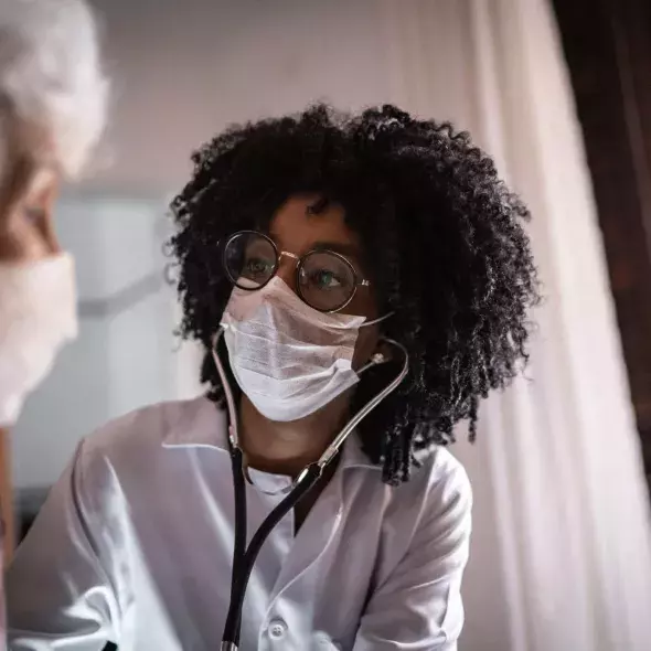 Masked Doctor Using Stethoscope with Patient