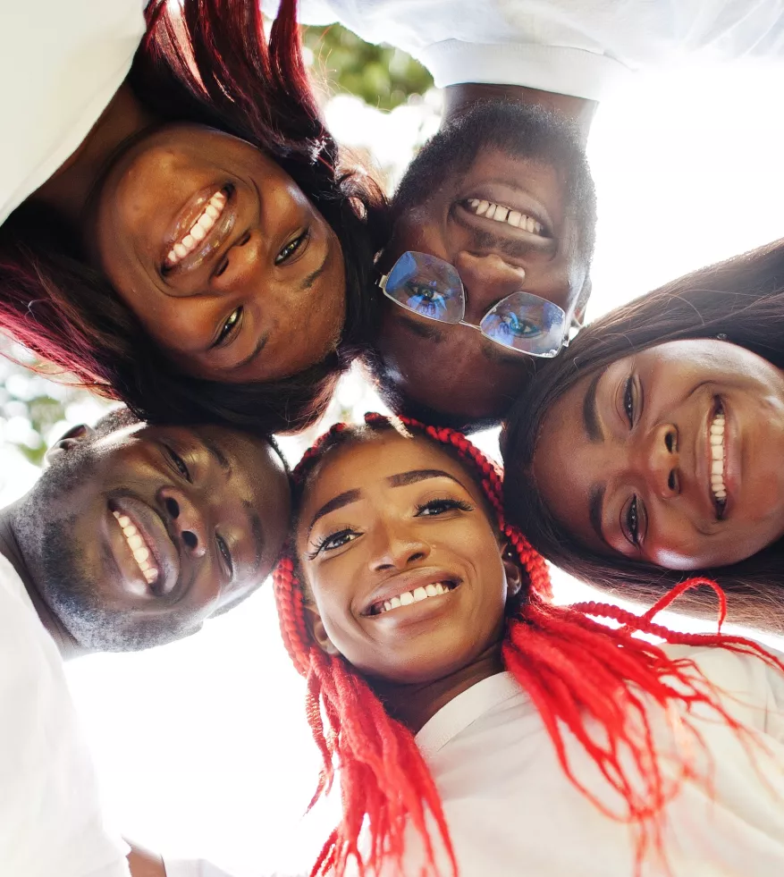 A group of Black people in white T-shirts smile together while in a huddle.