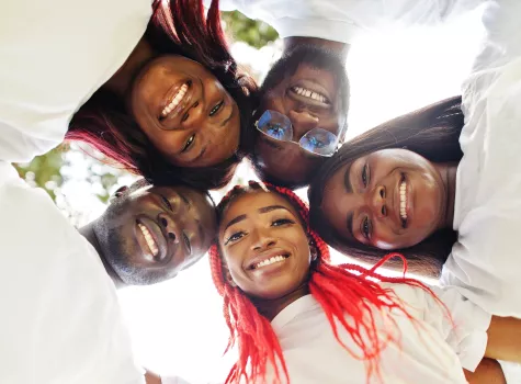 A group of Black people in white T-shirts smile together while in a huddle.