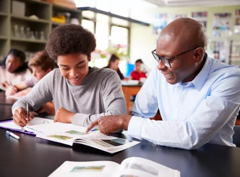 Smiling Black Teacher Instructing Student on Coursework in Classroom