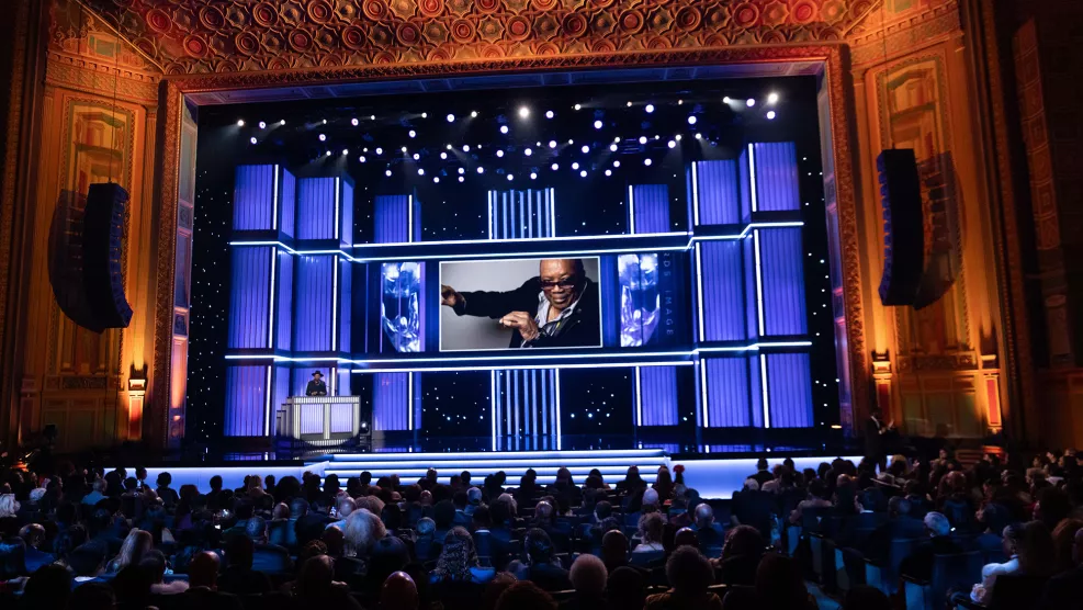 DJ D-Nice onstage during the 56th NAACP Image Awards with an image of Quincy Jones in the background.