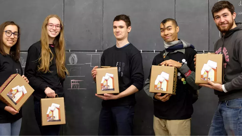 Five people stand in a row holding carboard boxes and smiling.