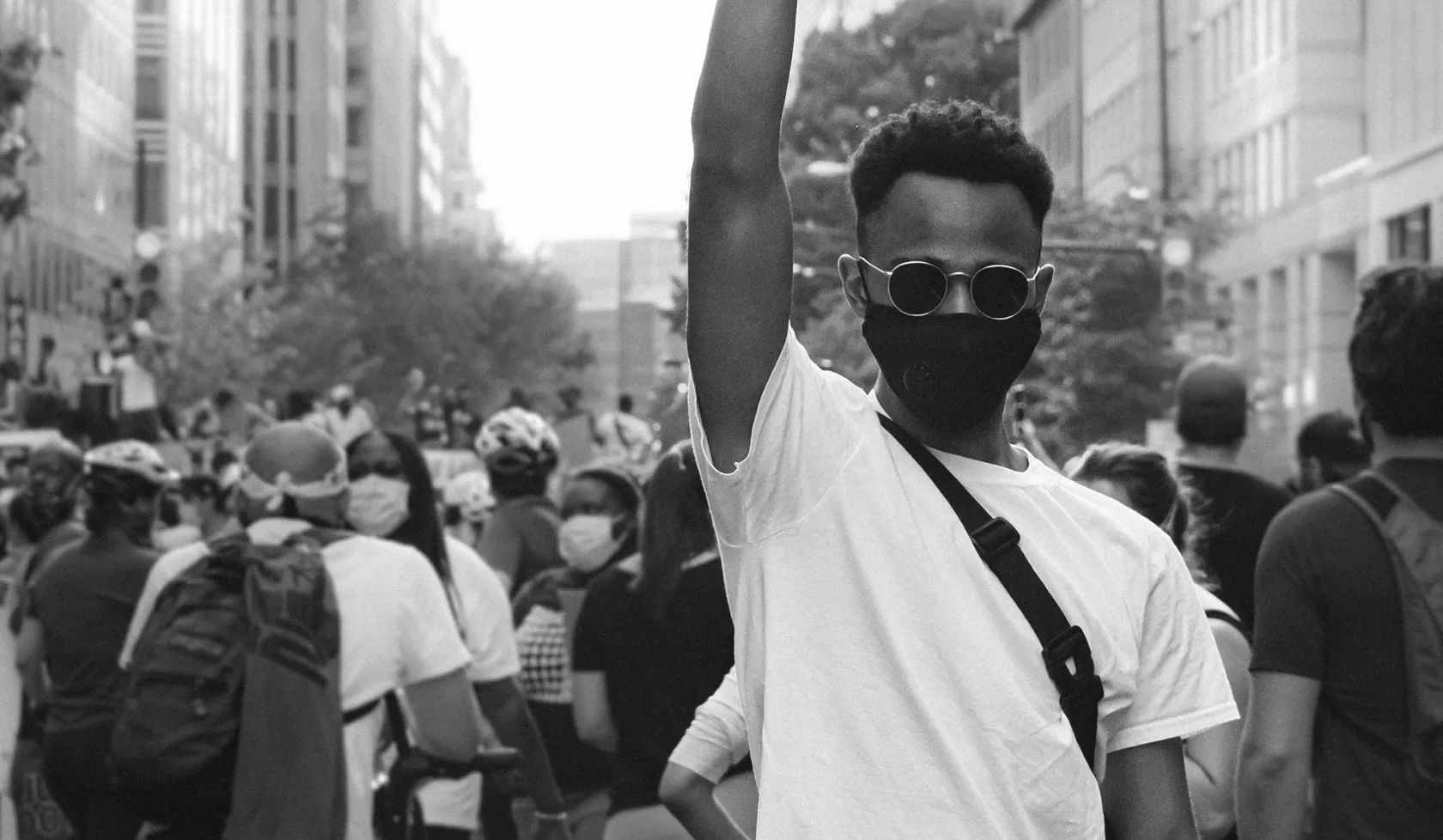 Black Male Outdoors - at protest or rally - group in background - raised fist - in face mask