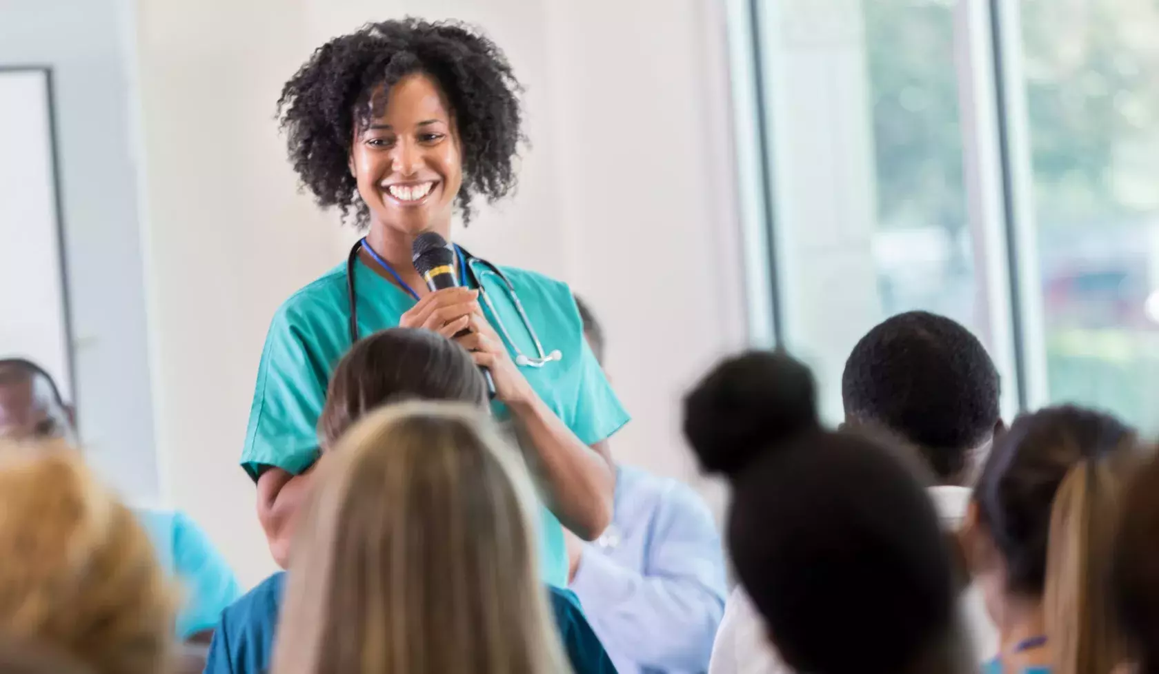 Smiling Black Female Health Professional Holding Microphone and Standing in Front of Audience