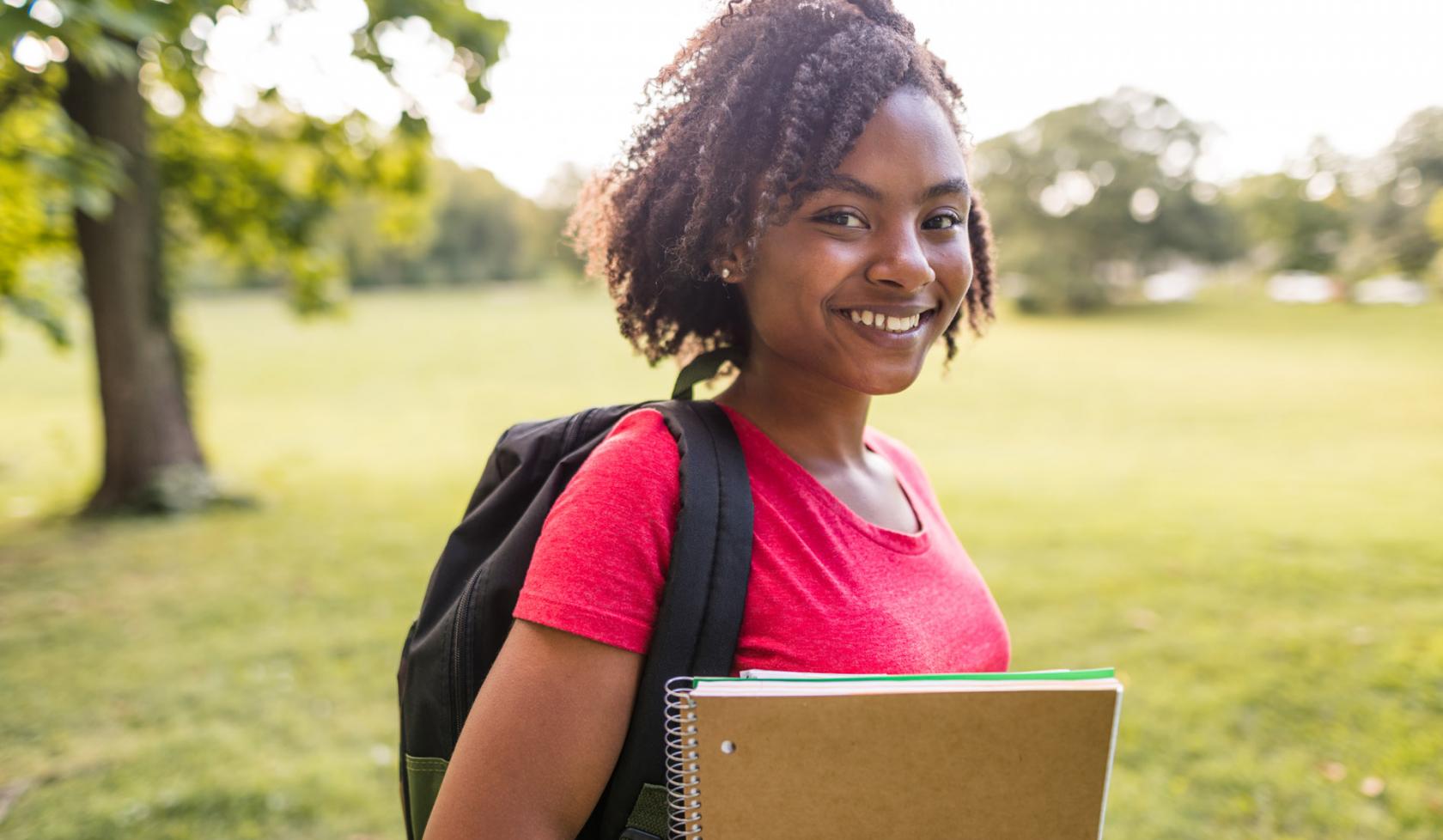 Smiling Young Black Female Student Wearing Backpack and Holding Books - Outdoors