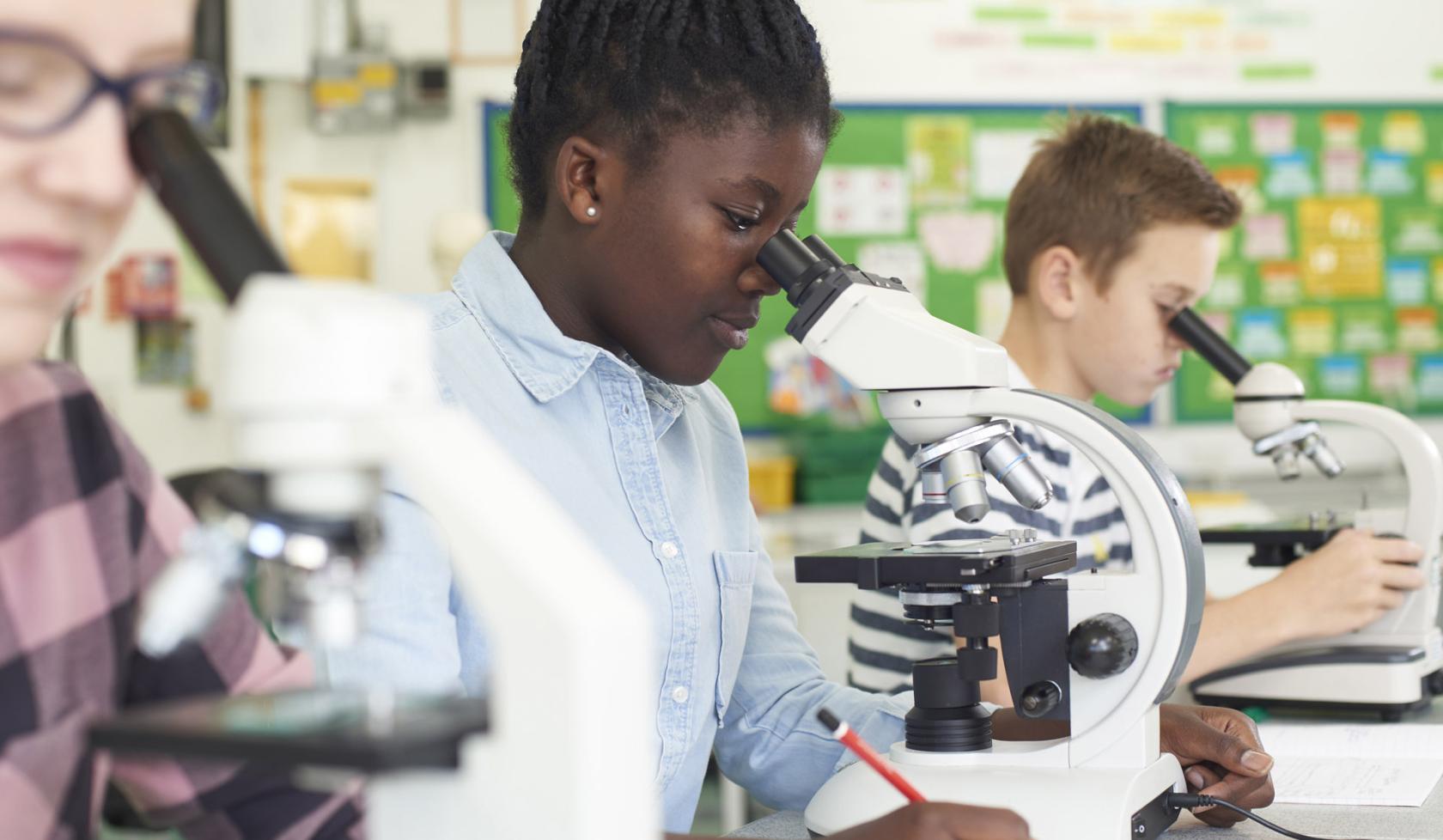 Close-up Young Black Female Student Looking into Microscope in Row of Classmates