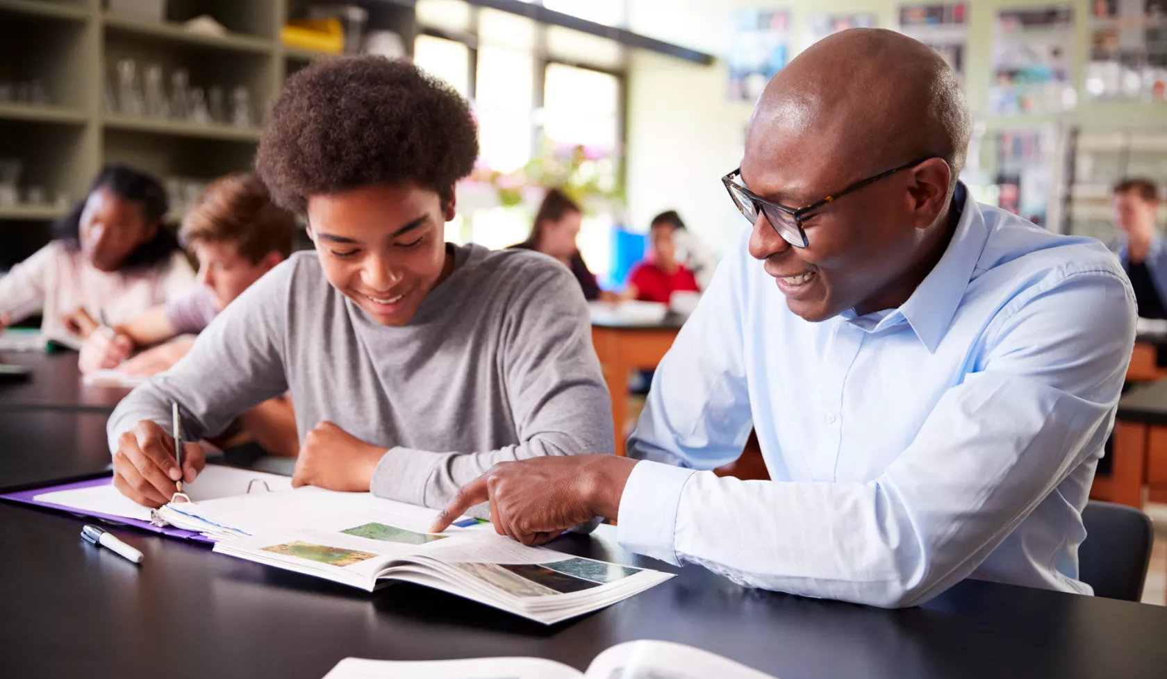 Smiling Black Teacher Instructing Student on Coursework in Classroom