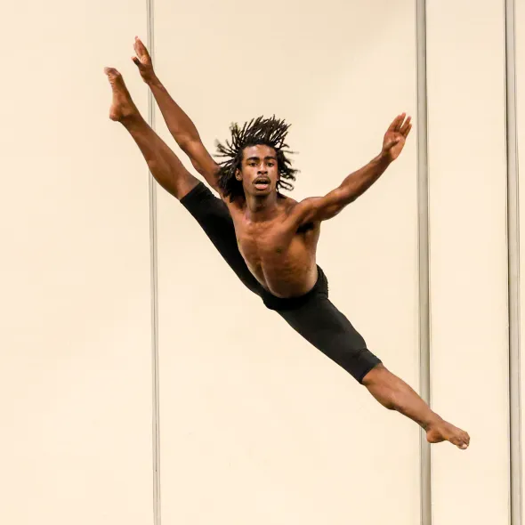 Black male dancer leaps through the air with a cream background