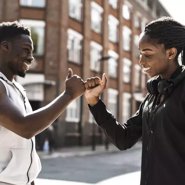 Smiling Black Young Man and Young Woman Linking Pinky Fingers Outside on Street