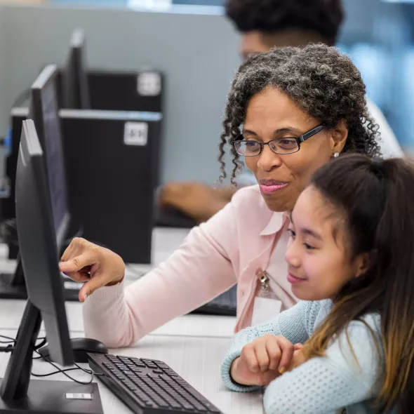 Female Teacher Instructing Young Student Using Computer