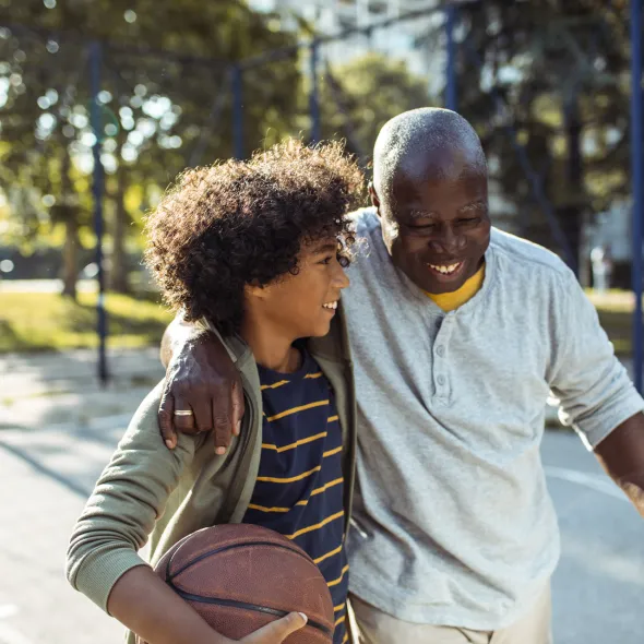 Smiling Grandfather Hugging Grandson on Outdoor Basketball Court