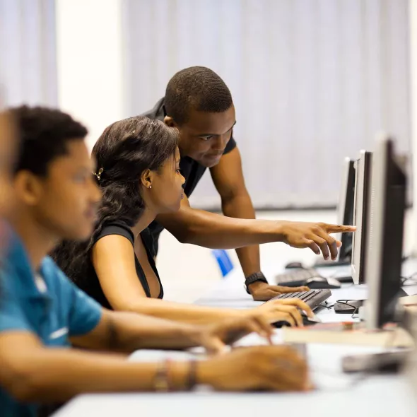 Young Black Man Helping A Female at a Computer - Classroom Setting