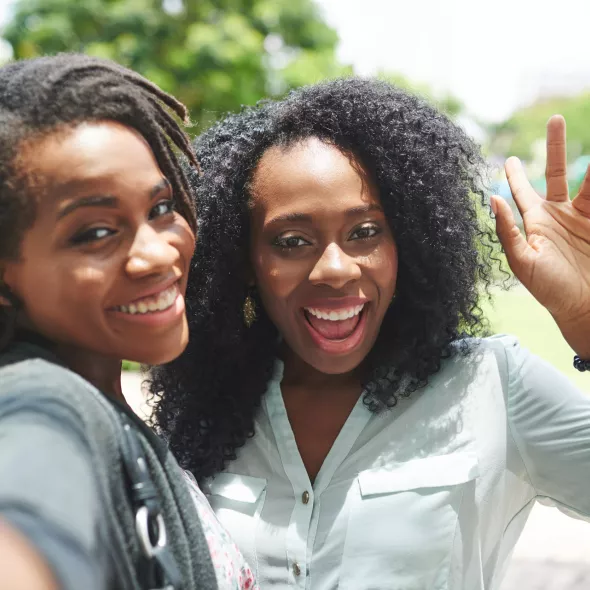 Two Grinning Black Women Taking a Selfie Together Outside
