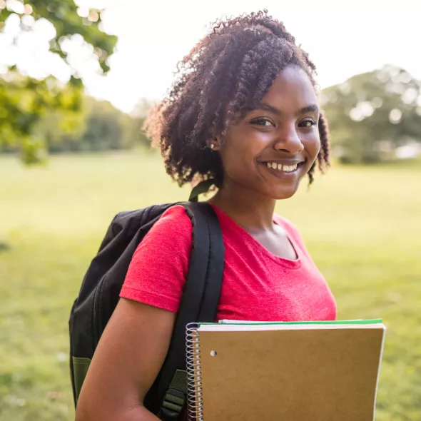 Smiling Young Black Female Student Wearing Backpack and Holding Books - Outdoors