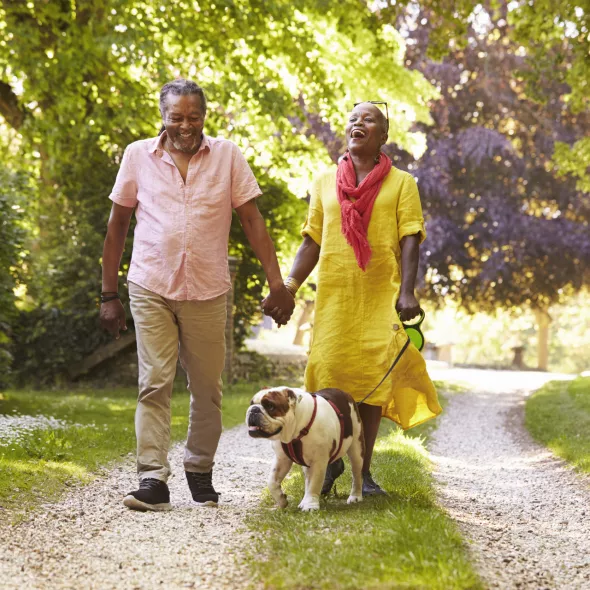 Senior Couple Smiling and Enjoying a Walk in the Park with their Dog