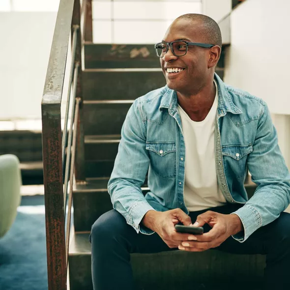 Black Male Sitting on Stairs Holding Phone - Smiling