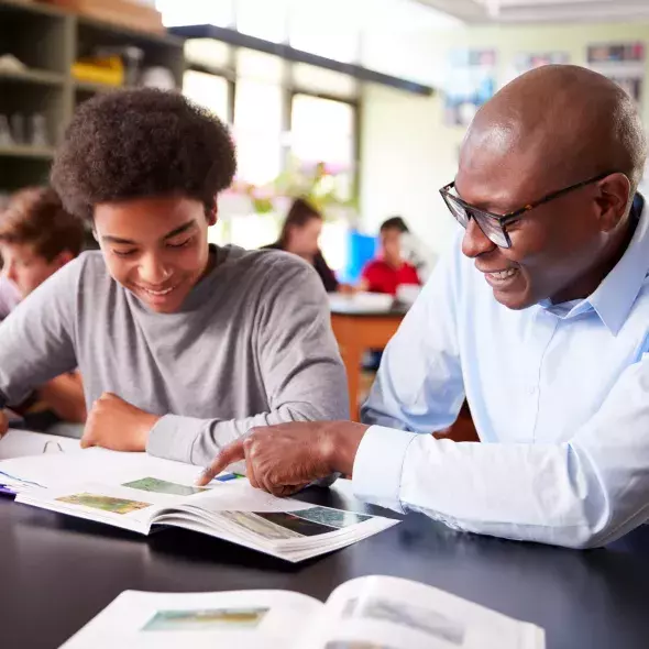 Smiling Black Teacher Instructing Student on Coursework in Classroom