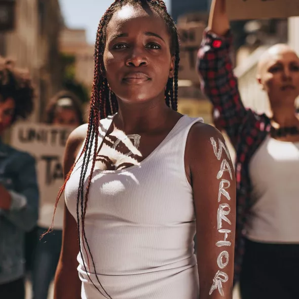 Black Female - Standing with Protestors - "Warrior" Painted on Her Arm