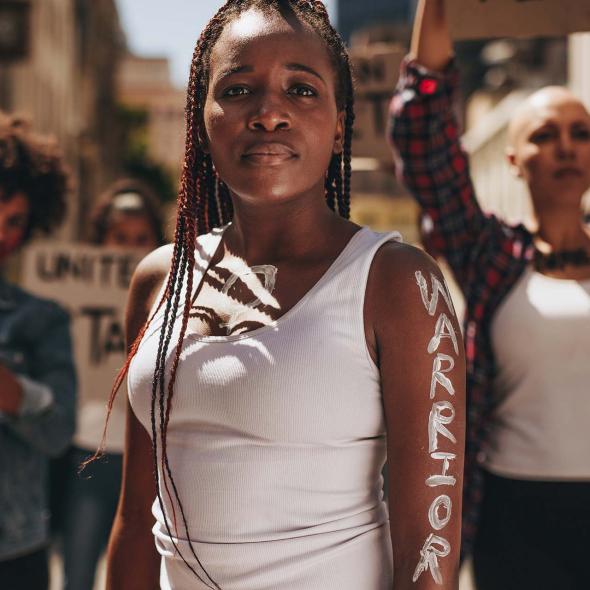 Black Female - Standing with Protestors - "Warrior" Painted on Her Arm