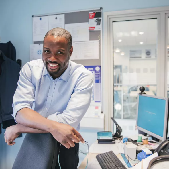 Smiling Black Teacher Alone in Office with Technology and View of Empty Classroom