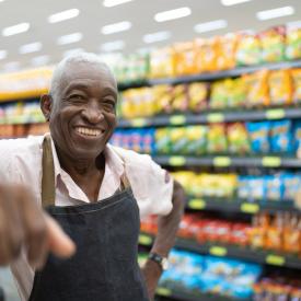 Senior Male Employee Smiling at Camera in Grocery Store Aisle