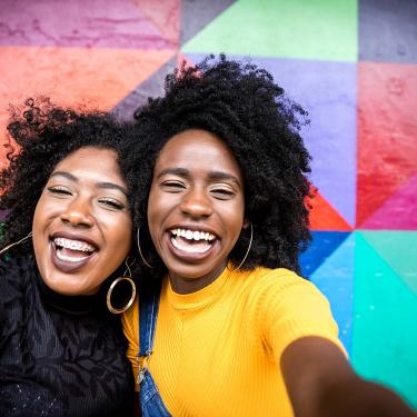 Two Young Black Females Smiling in Front of Colorful Outdoor Mural