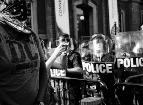 Police in riot gear - protestor in foreground - wearing face mask