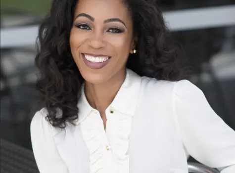 Ashley, an African American woman, smiles at the camera in a white button-down shirt. She has shoulder length dark brown hair.