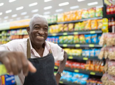 Senior Male Employee Smiling at Camera in Grocery Store Aisle