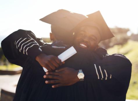 Two Black Male Graduates in Cap and Gown Hugging Each Other