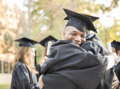 Happy Male Graduate Hugging Adult and Smiling at Camera