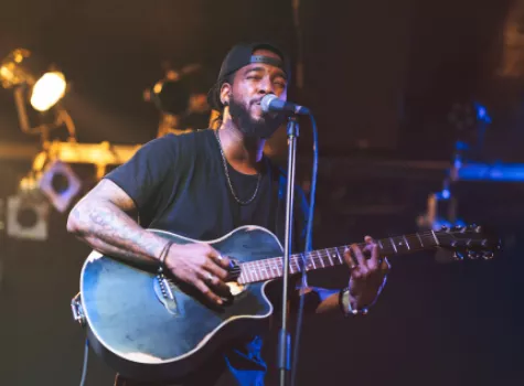 Close-up Black Male Performer on Stage Singing into Microphone and Playing Guitar