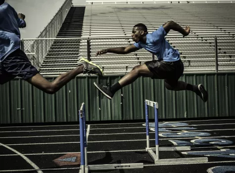 Black Athlete Jumping Over Hurdles on Track