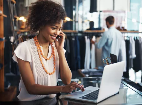 Woman Smiling and Talking into Phone and Working on Laptop in a Store Setting