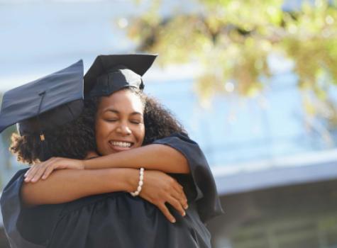Two Black Females in Graduation Caps - Hugging and Smiling