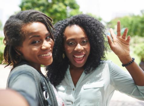 Two Grinning Black Women Taking a Selfie Together Outside