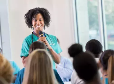 Smiling Black Female Health Professional Holding Microphone and Standing in Front of Audience
