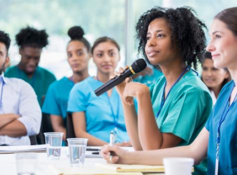 Black Female Medical Professional Holding Microphone Amongst a Group of Colleagues