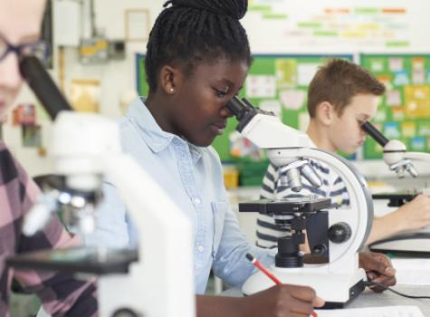Close-up Young Black Female Student Looking into Microscope in Row of Classmates