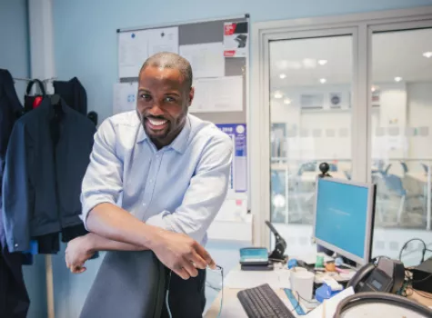 Smiling Black Teacher Alone in Office with Technology and View of Empty Classroom