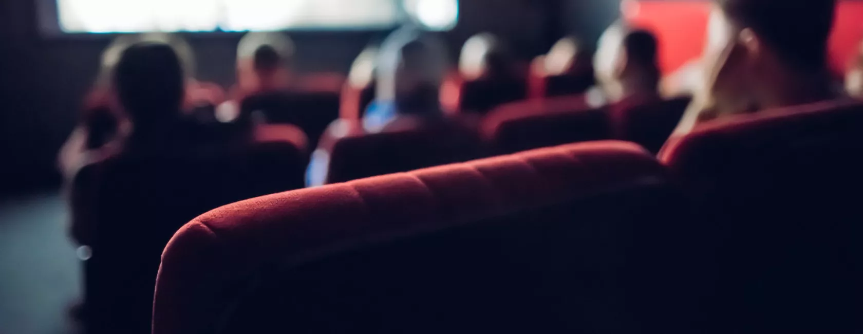 Blurred View of Red Velvet Seats in a Crowded Movie Theater
